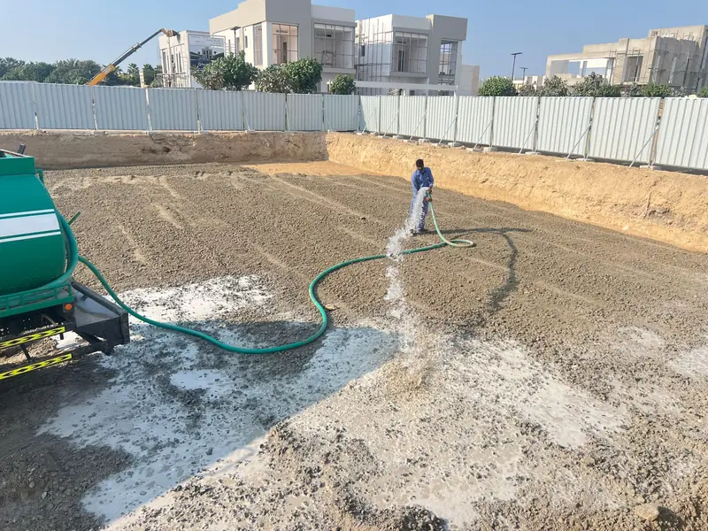 Site worker watering the excavation base before compaction at a villa site in Sharjah