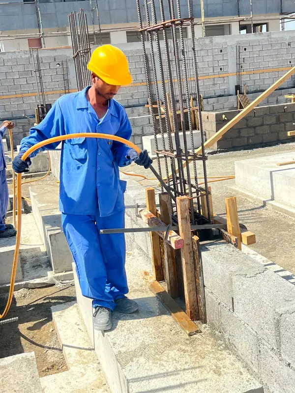 Worker curing concrete around column starter bars, villa construction in Sharjah